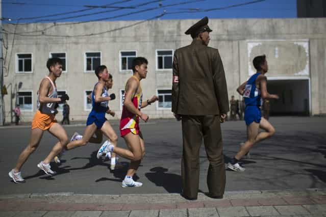 Marathon runners pass by a North Korean soldier during the race in Pyongyang on Sunday, April 14, 2013. North Korea hosted the 26th Mangyongdae Prize Marathon to mark the upcoming April 15, 2013 birthday of the late leader Kim Il Sung. (Photo by Alexander F. Yuan/AP Photo)
