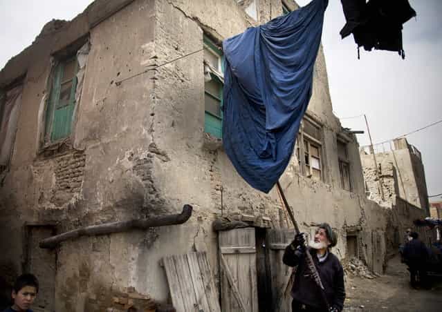 Haji Hussain, 75, who colors clothing for 40 years, takes a freshly colored burqa out for drying outside his small shop in the old town of Kabul, Afghanistan, Monday, April 15, 2013. (Photo by Anja Niedringhaus/AP Photo)