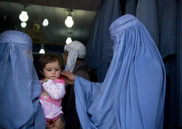 In this Thursday, April 11, 2013 photo. an Afghan woman comforts the child of her friend as both wait to get in line to try on a new burqa in a shop in the old town of Kabul, Afghanistan. (Photo by Anja Niedringhaus/AP Photo)