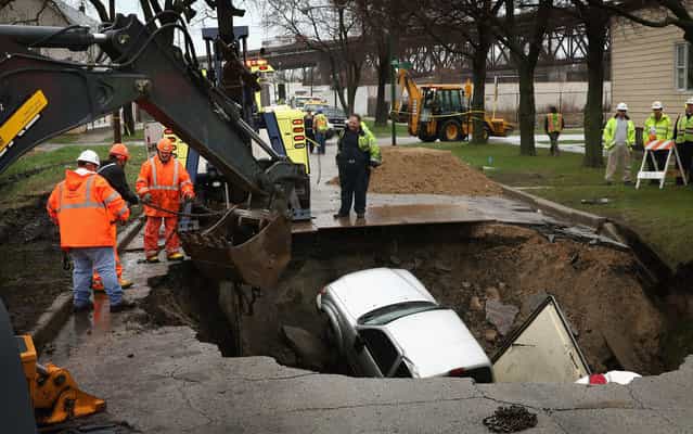 Workers prepare to pull a truck from a sinkhole that opened up on a residential street in the South Deering neighborhood on April 18, 2013 in Chicago, Illinois. The driver of the truck was hospitalized after driving into the 15-feet-deep hole while on his way to work. Two other vehicles were also swallowed by the sinkhole. (Photo by Scott Olson/AFP Photo)