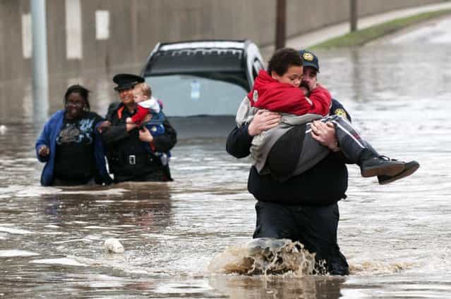 Firefighter Jason Kelley and police officer Shannon Vandenheuvel carry children from Barbara Jones' partially submerged car in Grand Rapids, Mich. Thursday, April 18, 2013. Middle America was getting everything nature has to throw at it on Thursday, from snow in the north to tornadoes in the Plains, and with torrential rains causing floods and transportation chaos in several states. (Photo by Chris Clark/AP Photo/Grand Rapids Press)