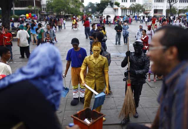 Visitors laugh as statue street performers pose as cleaning workers at Fatahilah museum park in Jakarta's old city April 14, 2013. As many as 10 statue performers gather at Fatahilah museum park on weekends to entertain visitors. (Photo by Reuters/Beawiharta)