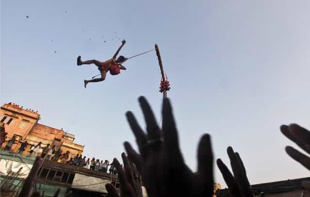 A Hindu devotee hanging from a rope throws offering towards other devotees during the [Chadak] ritual in Kolkata April 14, 2013. Hundreds of Hindu devotees attend the ritual, held to worship the Hindu deity of destruction Lord Shiva, on the last day of the Bengali calendar year. (Photo by Rupak De Chowdhuri/Reuters)