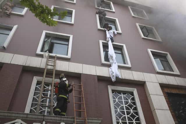 A firefighter holds a ladder as people climb down at the site of a hotel fire in Xiangyang, Hubei province, April 14, 2013. At least 11 people have been confirmed dead and 50 others injured in the fire on Sunday morning, Xinhua News Agency reported. (Photo by Reuters/China Daily)