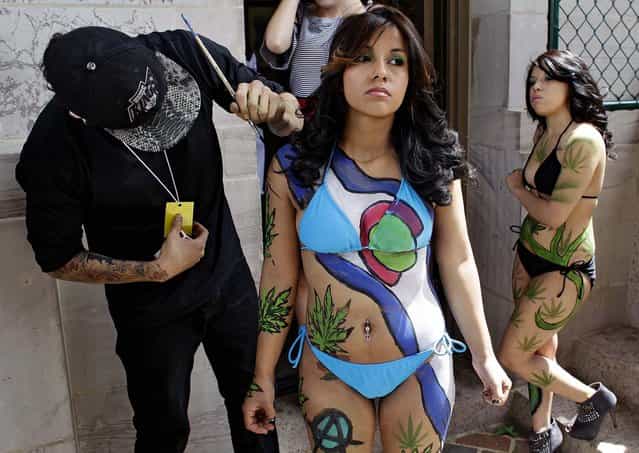 Tattoo artist Robert Duran touches up performer Ashley Lucero with a marijuana-themed body paint design, as Vanessa Pacheco looks on at right, at the Denver 4/20 pro-marijuana rally at Civic Center Park in Denver on Saturday, April 20, 2013. Even before the passage in November 2012 of Colorado Amendment 64 promised the legalization of marijuana for recreational use, April 20th has for years been a celebration of marijuana counterculture, with the 2013 Denver rally expected to draw larger crowds than previous years. (Photo by Brennan Linsley/AP Photo)