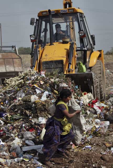 A young Indian rag carries bags filled with reusable materials as a backhoe pushes garbage at a dump yard on the outskirts of Jammu, India, Monday, April 22, 2013. April 22 is observed as Earth Day every year as a tool to raise ecological awareness. (Photo by Channi Anand/AP Photo)