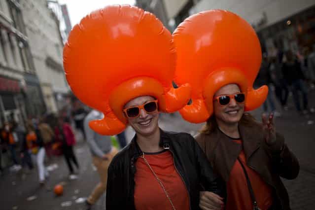 Two woman wearing inflatable caps walk along the street in Amsterdam, The Netherlands, Tuesday April 30, 2013. Around a million people are expected to descend on the Dutch capital for a huge street party to celebrate the first new Dutch monarch in 33 years. (Photo by Emilio Morenatti/AP Photo)