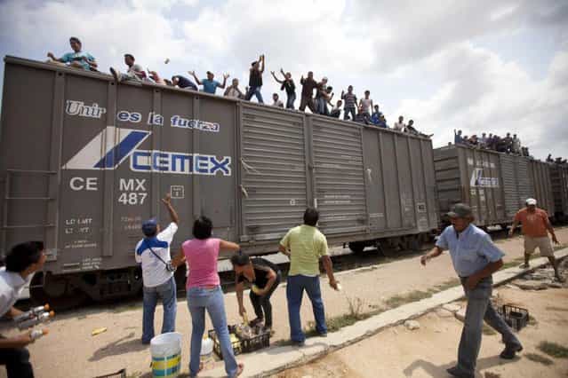 Residents toss food to migrants riding on top of a northern bound train toward the US-Mexico border, in Union Hidalgo, southern Mexico, Monday, April 29, 2013. Migrants crossing Mexico to get to the U.S. have increasingly become targets of criminal gangs who kidnap them to obtain ransom money. (Photo by Eduardo Verdugo/AP Photo)