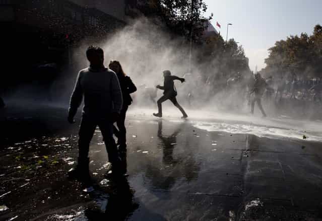 People walk through the spray of a police water cannon after clashes broke out between protesters and security forces at the annual May Day march in Santiago, Chile. (Photo by Luis Hidalgo/Associated Press)