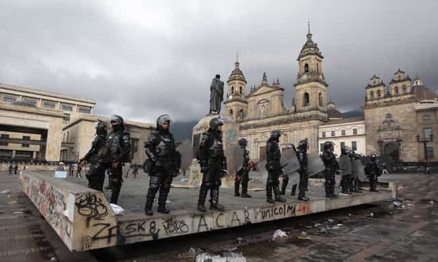 Riot police stand guard in Bolivar square after the annual May Day march ended in clashes in Bogota, Colombia, Wednesday, May 1, 2013. In protests, parades, strikes and other demonstrations held in cities across the planet, activists lashed out at political and business leaders they allege have ignored workers' voices or enriched themselves at the expense of laborers during what has been a difficult few years for the global economy. (Photo by Fernando Vergara/AP Photo)
