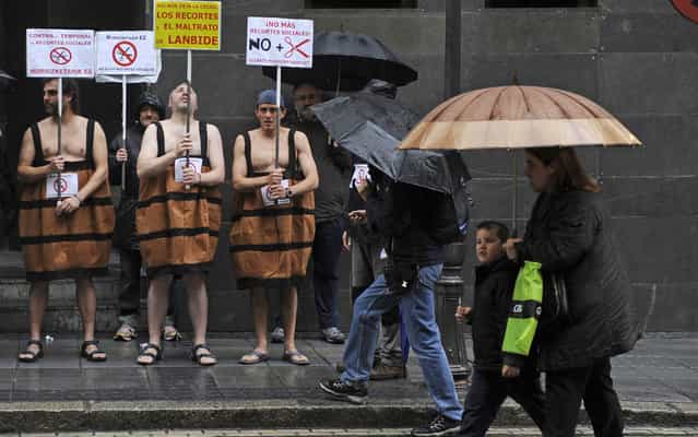 People walk past three men in barrel costumes holding placards against government’s social cuts during a protest called by several social groups in front of the ruling Basque Nationalist Party (PNV) headquarters in the northern Spanish city of Bilbao, on May 2, 2013. (Photo by Rafa Rivas/AFP Photo)
