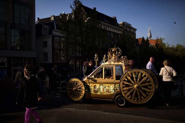 People walk past a car decorated as a royal carriage in Amsterdam, Netherlands, on April 28, 2013. Queen Beatrix announced she will relinquish the crown on April 30, after 33 years of reign, leaving the monarchy to her son Crown Prince Willem Alexander. (Photo by Emilio Morenatti/Associated Press)