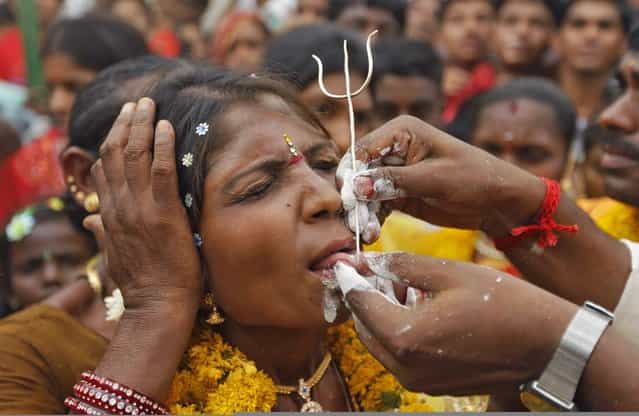 A Hindu devotee gets her tongue pierced with a trident as she takes part in an annual religious procession called Shitla Mata in the western Indian city of Ahmedabad April 29, 2013. Hindu devotees subject themselves to painful rituals during the religious procession to demonstrate their faith and as a penance to the deity at a temple dedicated to the goddess Shitla. (Photo by Amit Dave/Reuters)