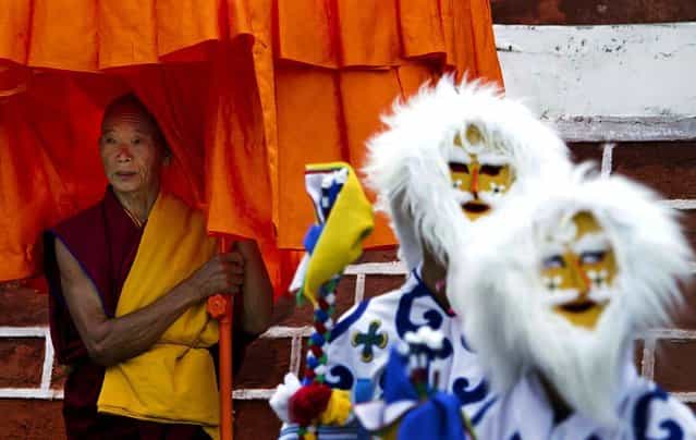 A Tibetan Buddhist monk waits with masked dancers to welcome the Dalai Lama at the Central School for Tibetans in Dalhousie, India, on April 27, 2013. (Photo by Ashwini Bhatia/Associated Press)