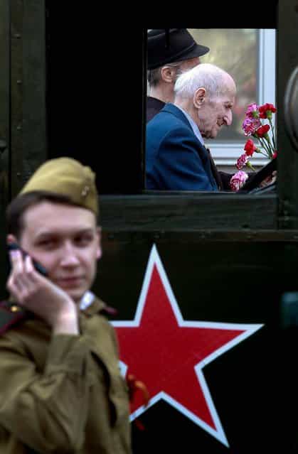 World War II veterans ride a car as a member of a historical military club wearing Soviet army uniform speaks on a phone during the celebration of Victory Day in St. Petersburg, Russia. (Photo by Dmitry Lovetsky/Associated Press)