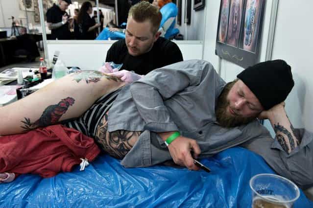 Christian Funch writes a text message whilst being tattooed by Mikkel Westrup from Good Times Tattoo, Thursday May 9. 2013 in Copenhagen, Denmark, during the third Copenhagen Ink Festival, the biggest tattoo festival in Northern Europe. During the three days, 180 of the world's best and most celebrated national and international tattoo artists show the audience their skills in making art on the body and tattoo's on the audience. (Photo by Lars Krabbe/AP Photo)
