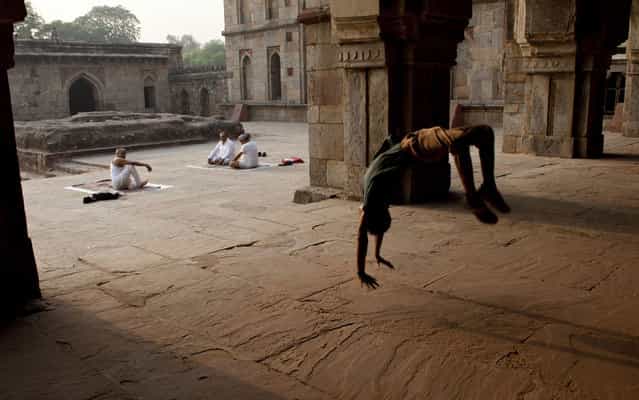 A young dancer practicing pirouettes while participants performed yoga exercise at the bottom in front of the Mosque of Three Domes in Lodi Gardens in New Delhi, India, on May 7, 2013. (Photo by Tengku Bahar/AFP Photo)