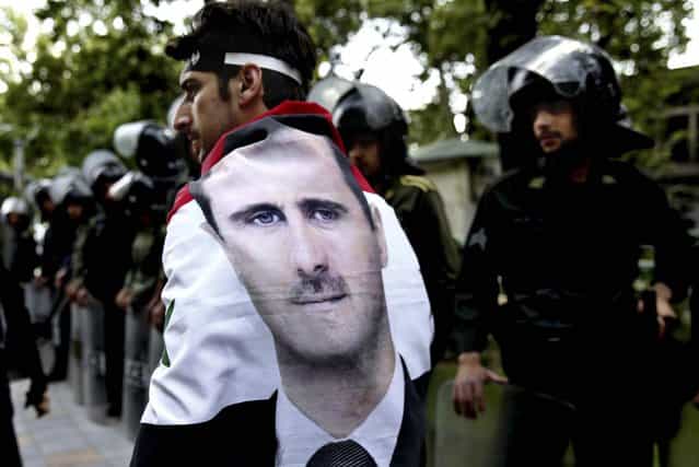 A man wrapped in a Syrian flag with a portrait of President Bashar Assad, walks past riot police at an anti-Israeli demonstration in front of the UN office in Tehran, on May 6, 2013. Iran condemns Israeli Air strikes on Syria and urged countries in the region to stand against the attack. (Photo by Ebrahim Noroozi/Associated Press)