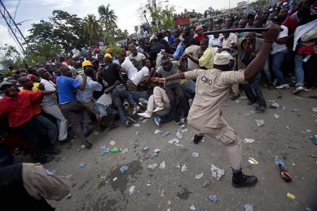 A police officer uses his baton to beat back supporters of Haiti's former President Jean-Bertrand Aristide who gathered outside the courthouse where Aristide arrived earlier in the day, in Port-au-Prince, on May 8, 2013. The two-time president showed up at the courthouse to testify before a judge investigating the 2000 slaying of Jean Dominique, one of the Caribbean country's most prominent journalists. (Photo by Dieu Nalio Chery/Associated Press)