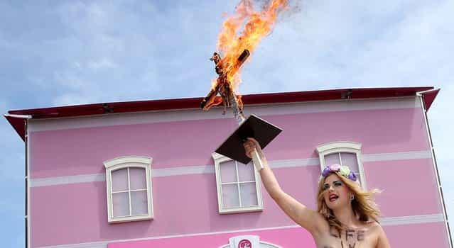 A bare-breasted FEMEN protester, with an inscription on her body that reads: [Life In Plastic Is Not Fantastic], holds up a burning cross with a Barbie doll attached to it outside the Barbie Dreamhouse Experience in Berlin, on May 16, 2013. (Photo by Sean Gallup/Getty Images)