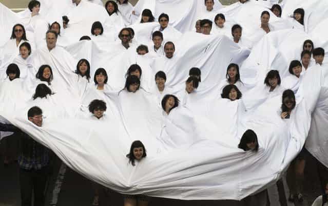 Participants, with their heads sticking out from holes of a large white fabric, perform during a performance, [Divisor] during an exhibition, [A Journal of the Plague Year. Fear, Ghosts, Rebels. SARS, Leslie and the Hong Kong Story], in Central business district of Hong Kong Friday, May 17, 2013. The art work was originally performed on the streets of Rio de Janeiro in 1968, created by the Late Brazilian artist Lygia Pape. (Photo by Kin Cheung/AP Photo)