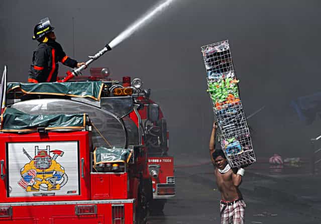 A Filipino vendor recovers items as a firefighter directs a water hose towards a burning shopping mall in Manila, Philippines, 16 May 2012. A fire that broke out early 16 May at the Divisoria Mall could take days to put out, estimated firefighters. (Photo by Francis R. Malasig/EPA)