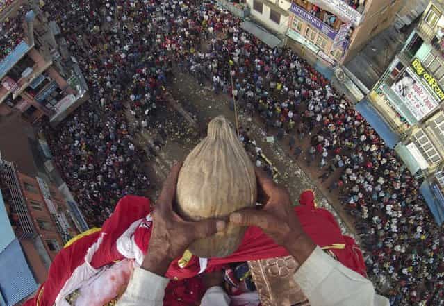 Chakala Dangol, 75, holds a coconut on his hand before throwing it towards the devotees from the top of the chariot of Rato during the chariot festival in Lalitpur May 21, 2013. It is believed that whoever grabs the coconut and returns it to the chariot will be blessed with a son. Rato Machhindranath is known as the god of rain and both Hindus and Buddhists worship Machhindranath for good rain to prevent drought during the rice harvest season. (Photo by Navesh Chitrakar/Reuters)