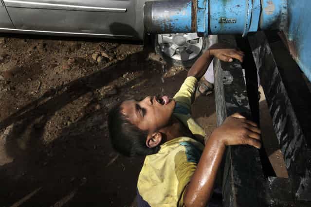 An Indian boy drinks water dripping from a government tanker supplying water to residents of a colony in New Delhi, India, Thursday, May 23, 2013. Many areas of the Indian capital are facing acute water shortage, a repeated annual phenomenon during summer when taps go dry as demand rises. (Photo by Manish Swarup/AP Photo)