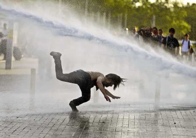 A man falls as riot police use tear gas and pressurized water to quash a peaceful demonstration by hundreds of people staging a sit-in protest to prevent the demolition of trees at an Istanbul park, on May 31, 2013. (Photo by Associated Press)