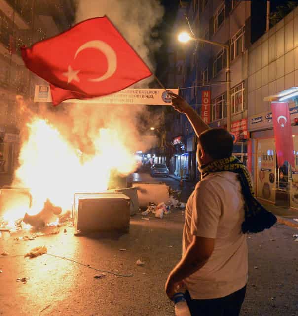In this photo taken late Saturday, June 1, 2013, a demonstrator waves a national flag as Turkish protesters clash with riot police near the former Ottoman palace, Dolmabahce, where Turkey's Prime Minister Recep Tayyip Erdogan maintains an office in Istanbul, Turkey. (Photo by AP Photo)