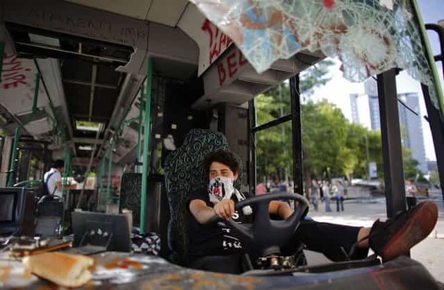 A Besiktas soccer fan uses his team's scarf as a mask while sitting in a damaged bus at Taksim Square in central Istanbul June 4, 2013. Days of anti-government protest in Turkey have achieved one feat that has eluded the authorities for years: uniting the fiercely rival and sometimes violent supporters of Istanbul's [Big Three] football clubs. Besiktas, Galatasaray and Fenerbahce fans have come together in new-found solidarity during five days of demonstrations against Prime Minister Tayyip Erdogan's government. (Photo by Murad Sezer/Reuters)