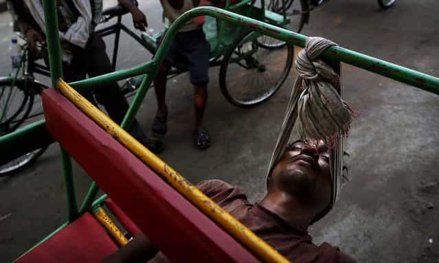 A bicycle rickshaw walla uses a scarf to rest his head while sleeping on his rickshaw in New Delhi, on June 6, 2013. Many of the men who make their living driving clients through the busy streets of the Indian capital sleep on their rickshaws, both to guard them and because they are from other parts of the country and have no permanent residence. (Photo by Kevin Frayer/Associated Press)
