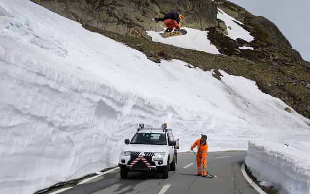 Snowboarder Sebastien Jam jumps above a roadman during a photo shooting on June 12, 2013 on the road of the Grand-Saint-Bernard pass. The road maintenance the canton of Valais is taking off the last snow on the 2473 meters high mountain pass after exceptional snowfalls in recent months. Connecting Switzerland and Italy, the Grand-Saint-Bernard pass is due to reopen for the summer season with two week delay on June 14, 2013. (Photo by Fabrice Coffrini/AFP Photo)