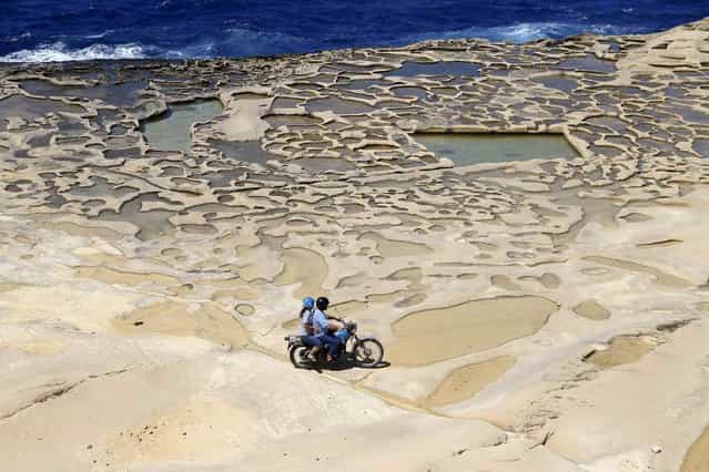 A man and his passenger ride a motorcycle near salt pans, believed to have been used for harvesting sea salt since Roman times, outside the village of Marsalforn, on the northern coast of the Maltese island of Gozo, June 12, 2013. (Photo by Darrin Zammit Lupi/Reuters)
