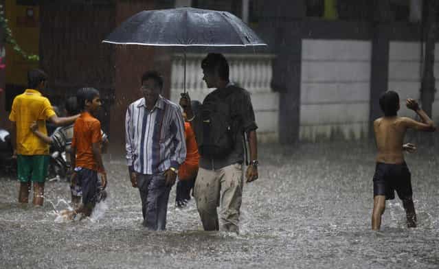 Children play as two men walk through a flooded street during monsoon rains in Mumbai, India, Sunday, June 9, 2013. The Southwest monsoon, arrived in the city Saturday, three days ahead of schedule, according to the meteorological department. (Photo by Rafiq Maqbool/AP Photo)