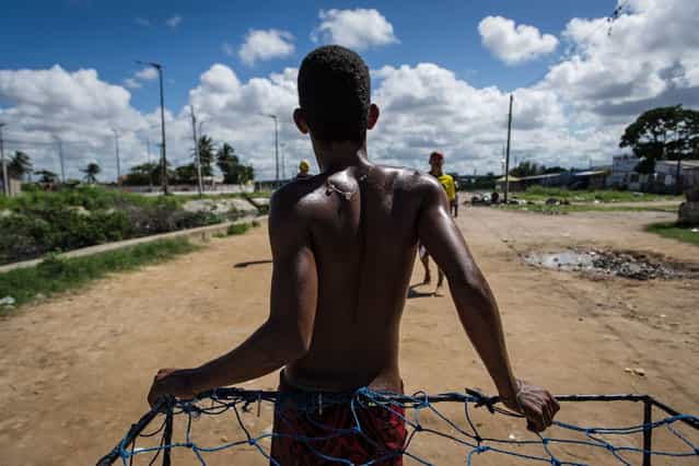 A young man leans on a handmade goal as he plays football in a shantytown of Olinda, about 18 km from Recife in northeastern Brazil, on June 18, 2013 as the FIFA Confederations Cup Brazil 2013 football tournament is being held in the country. The historic centre of Olinda is listed as an UNESCO World Heritage Site. (Photo by Yasuyoshi Chiba/AFP Photo)