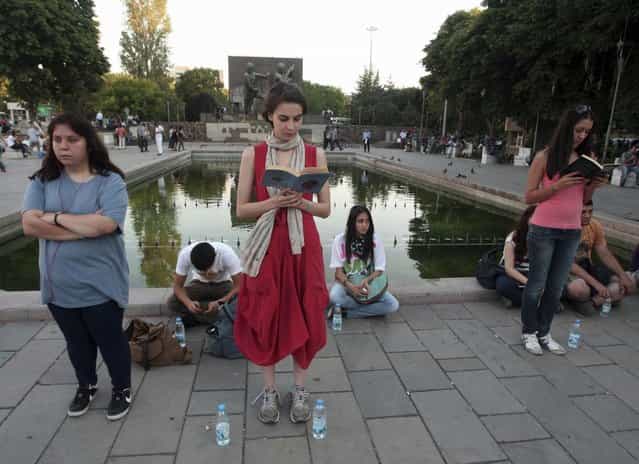 In this photo taken Tuesday, June 18, 2013, a woman stands in a silent protest as others read at Kizilay Square in Ankara, Turkey. After weeks of sometimes-violent confrontation with police, Turkish protesters have found a new form of resistance: standing still and silent. (Photo by AP Photo)