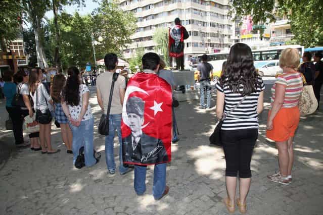 Protesters, one wearing a national flag with an image of Turkey's founder Kemal Ataturk, stand in a silent protest in Kugulu Park in Ankara, Turkey, Wednesday, June 19, 2013. After weeks of sometimes-violent confrontation with police, Turkish protesters have found a new form of resistance: standing still and silent. (Photo by Burhan Ozbilic/AP Photo)
