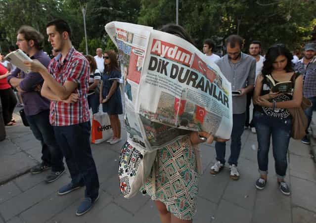 A woman reads a newspaper with the headline reading [Standing men], during a silent protest in Guven Park in Ankara, Turkey, Wednesday, June 19, 2013. After weeks of sometimes-violent confrontation with police, Turkish protesters have found a new form of resistance, standing still and silent. (Photo by Burhan Ozbilic/AP Photo)