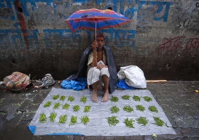 A vegetable vendor sits under an umbrella on a tarpaulin sheet at a market during monsoon rains in Mumbai June 18, 2013. The rains are at least twice as heavy as usual in northwest and central India as the June-September monsoon spreads north, covering the whole country a month faster than normal. (Photo by Vivek Prakash/Reuters)