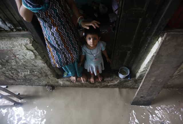 A child watches while standing on the doorstep of her house next to a flooded alley due to rising water level of river Yamuna after heavy monsoon rains in New Delhi June 18, 2013. The rains are at least twice as heavy as usual in northwest and central India as the June-September monsoon spreads north, covering the whole country a month faster than normal. (Photo by Anindito Mukherjee/Reuters)