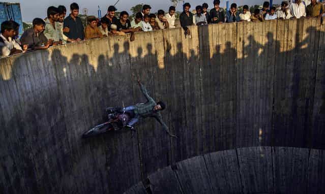 People watch as an acrobat rides his motorcycle around a circular track at an entertainment park set up outside a shrine in Rawalpindi, Pakistan, on June 19, 2013. (Photo by Muhammed Muheisen/Associated Press)