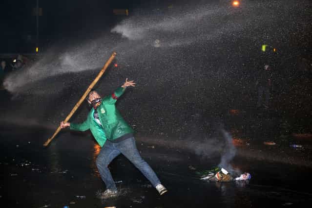 An Indonesian student hurls a bamboo stick as police spray a water cannon during a protest against the fuel price hike outside parliament in Jakarta on June 17, 2013. Police fired tear gas and rubber bullets at stone-throwing protesters in Indonesia on June 17, as thousands demonstrated nationwide against the government's plan to increase fuel prices. (Photo by Adek Berry/AFP Photo)