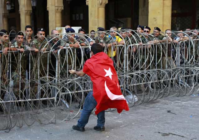 A civil society protester tries to remove barbed wire while wearing a Turkish flag during a demonstration protesting the extension of parliament's mandate, near Parliament in Beirut, Lebanon, Friday, June 21, 2013. Lebanon's parliament on May 29 extended its term by a year and a half, skipping scheduled elections because of the country's deteriorating security linked to the civil war next door in Syria. (Photo by Bilal Hussein/AP Photo)