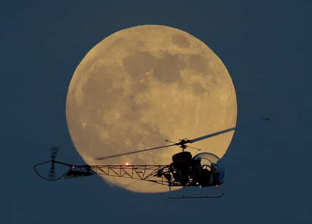 The moon is seen in its waxing gibbous stage as it rises behind the helicopter from the original Batman television show, which people can ride at the New Jersey State Fair, Saturday, June 22, 2013, in East Rutherford, N.J. The moon, which will reach its full stage on Sunday, is expected to be 13.5 percent closer to earth during a phenomenon known as supermoon. (Photo by Julio Cortez/AP Photo)