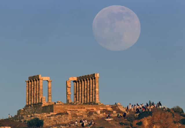 The moon rises over the temple of Poseidon, the ancient Greek god of the seas, as tourists enjoy the sunset in Cape Sounion some 60 km east of Athens June 22, 2013. The moon will reach its full stage on Sunday, and is expected to be 13.5 percent closer to earth during a phenomenon known as supermoon. (Photo by Yannis Behrakis/Reuters)