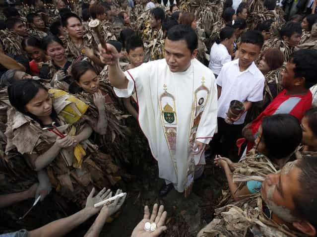 A priest sprinkles holy water on people, covered with mud and dried banana leaves, during a mass celebrating the feast day of the Catholic patron Saint John the Baptist in the village of Bibiclat, Nueva Ecija, north of Manila, June 24, 2013. Hundreds of devotees took part in this annual religious tradition, which has been held in the village since 1945. (Photo by Cheryl Ravelo/Reuters)