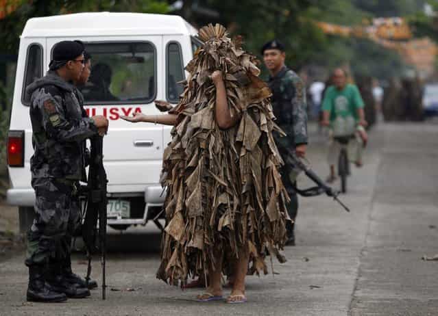 Residents, covered with mud and dried banana leaves, ask for money and candles from police before attending a mass celebrating the feast day of the Catholic patron Saint John the Baptist in the village of Bibiclat, Nueva Ecija, north of Manila, June 24, 2013. Hundreds of devotees took part in this annual religious tradition, which has been held in the village since 1945. (Photo by Cheryl Ravelo/Reuters)