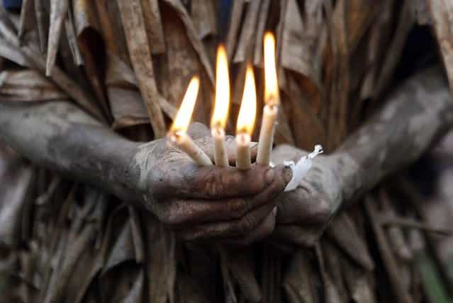 A resident, covered with mud and dried banana leaves, hold candles as he attends a mass celebrating the feast day of the Catholic patron Saint John the Baptist in the village of Bibiclat, Nueva Ecija, north of Manila, June 24, 2013. Hundreds of devotees took part in this annual religious tradition, which has been held in the village since 1945. (Photo by Cheryl Ravelo/Reuters)