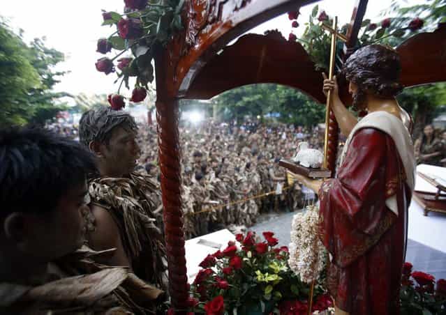 An image of Catholic patron Saint John the Baptist is displayed as residents, covered with mud and dried banana leaves, attend a mass celebrating the feast day in the village of Bibiclat, Nueva Ecija, north of Manila, June 24, 2013. Hundreds of devotees took part in this annual religious tradition, which has been held in the village since 1945. (Photo by Cheryl Ravelo/Reuters)